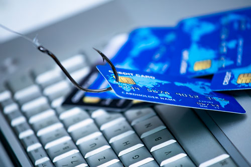 Fishing hooked onto a credit card hanging over computer keyboard