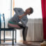woman practicing yoga using chair, doing Revolved Chair Pose, in the living room at home