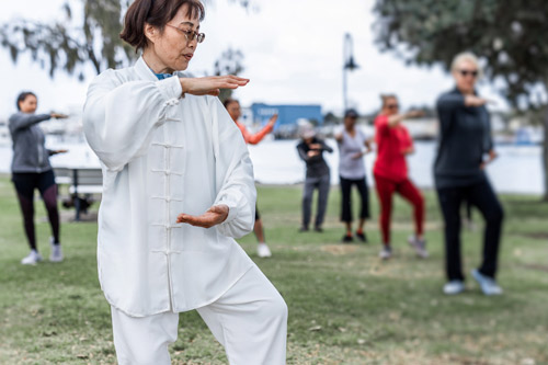qigong woman doing tai chi with blurred group of people outdoor in the park