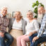 four elderly people sitting in a circle in a living room with a plant in the background