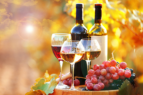 glasses of red and white wine on a table with bottles and grapes outdoors