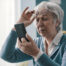 Woman wearing a blue sweater holds a phone to read, with glasses resting on her head