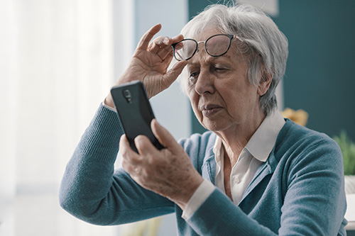 Woman wearing a blue sweater holds a phone to read, with glasses resting on her head