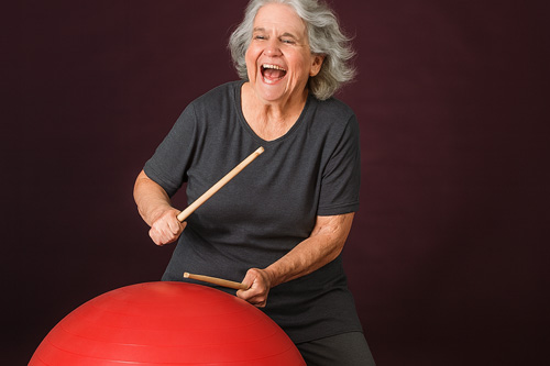 older woman happily drumming on medicine ball